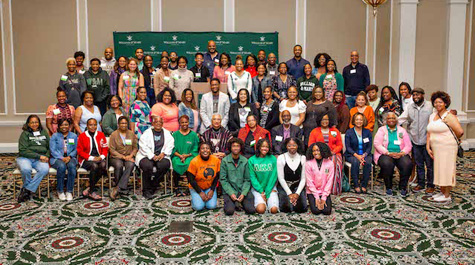 A group of people pose for a photo in front of a green backdrop that says William & Mary