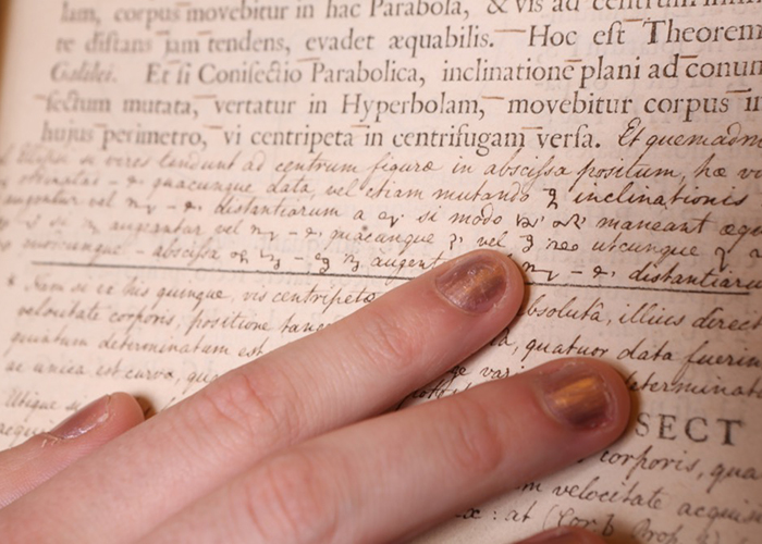 Hand pointing at hand-written notes on a yellowed book page