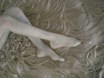 sculpture of woman's feet and legs on bed of white hair