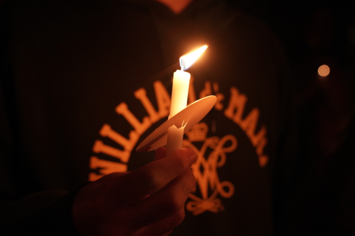 Candle held in hand with William & Mary and cypher on sweatshirt behind it worn by person holding it