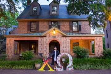 Someone stands by a large Xo and O in front of a brick house with a large front porch