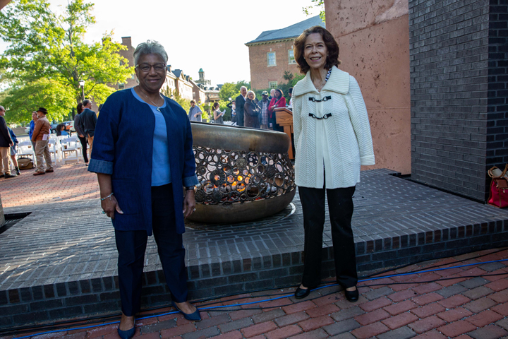 Two people stand by a sculpture that holds a flame