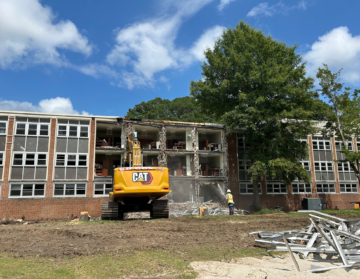 A piece of construction equipment demolishes a multi-story brick building