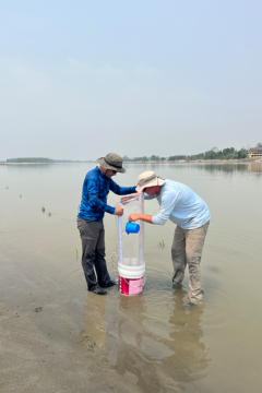 Two people pour water through a filter and into a bucket