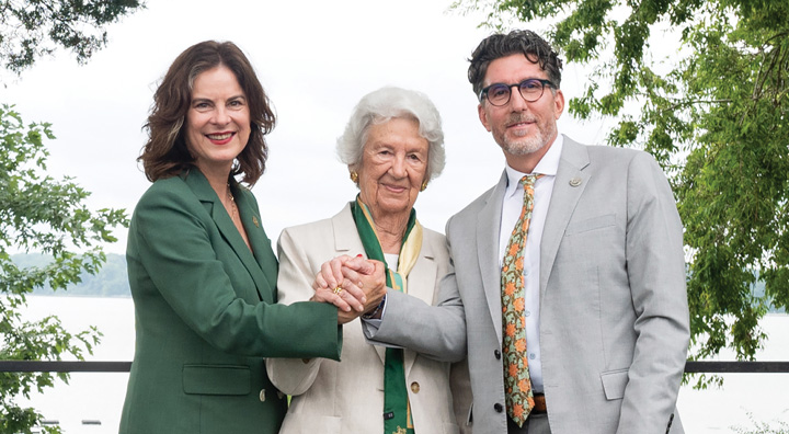 Three people clasp hands while standing near a body of water.