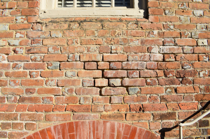 Bricks on a wall appear worn and missing mortar.