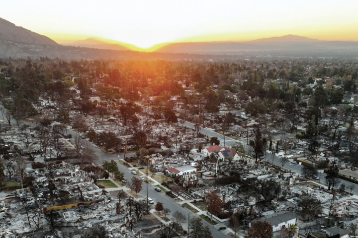 The sun sets over mountains near a neighborhood where houses and other structures have burned.
