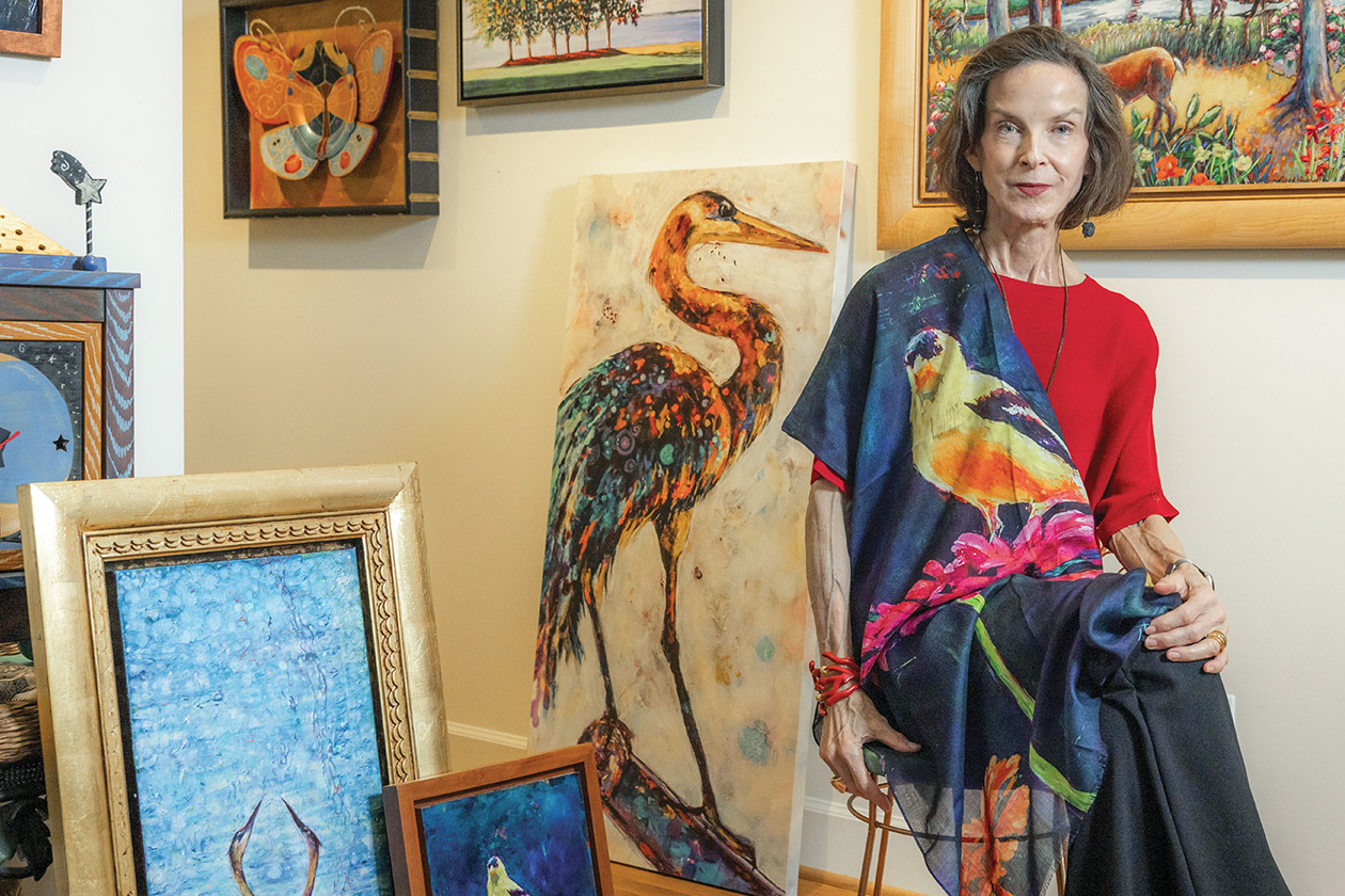 A person wearing bright clothing sits on a stool near several artworks on the floor and walls.