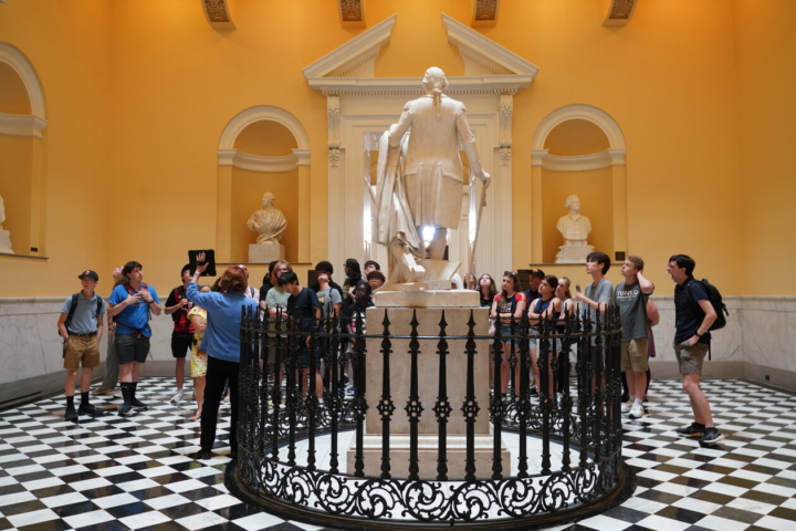 A gather of students circle around a marble statue of George Washington.