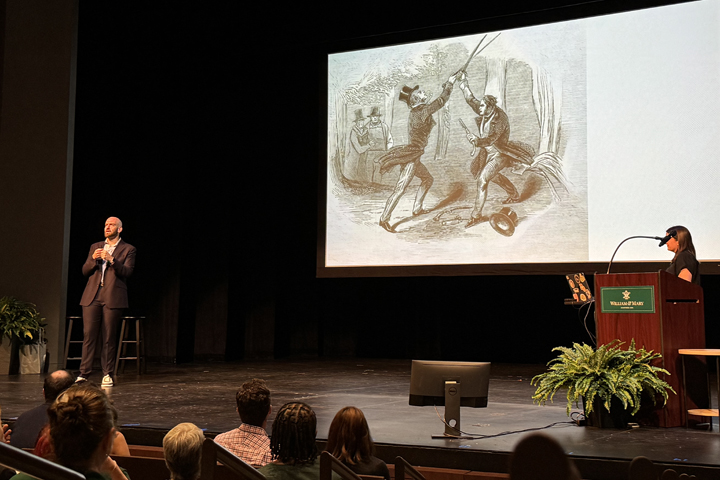 Two people stand on a stage near a screen that shows a black and white sketch of two people sword fighting.