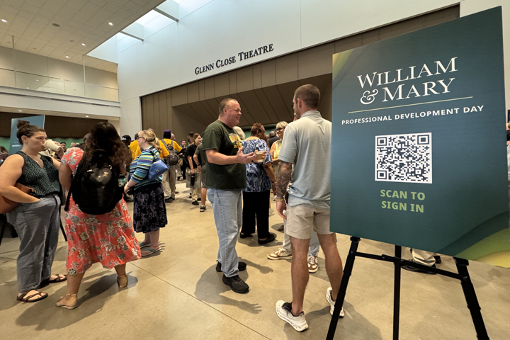 People talk to one another while standing near an entrance to a theater and by a sign that says William & Mary Professional Development Day.
