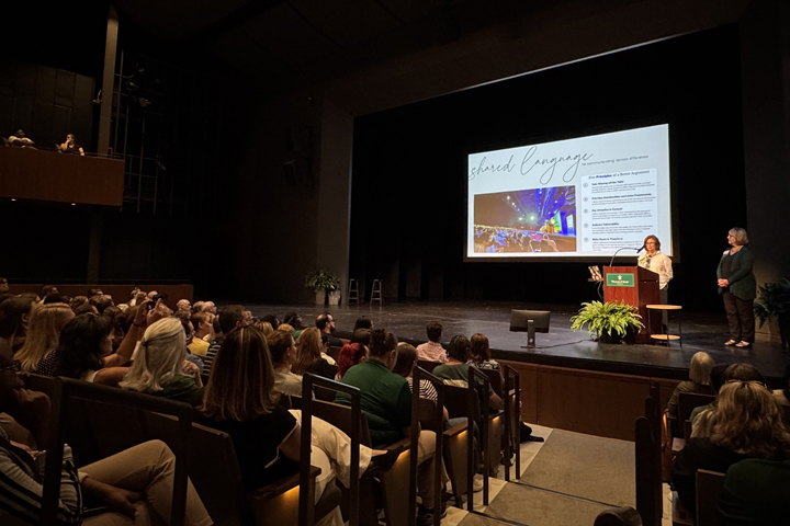 Two people stand at a podium on a stage near a screen that says "Shared language."