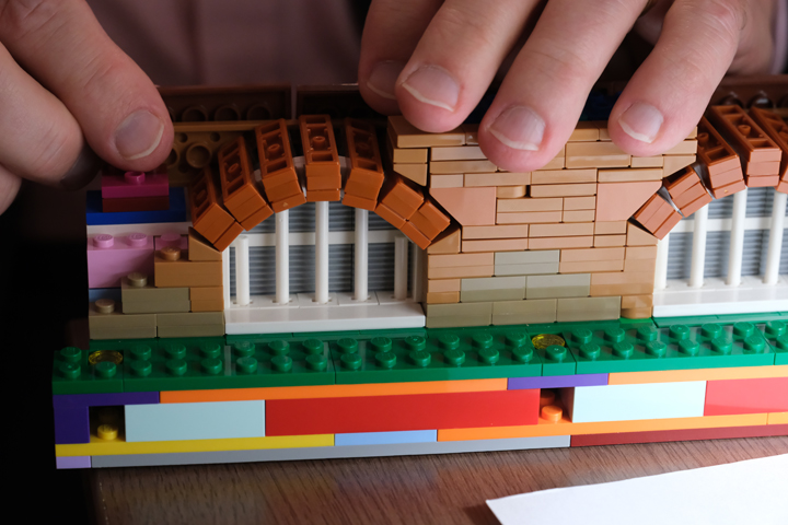 A person's fingers touch a Lego piece that shows a curved window.
