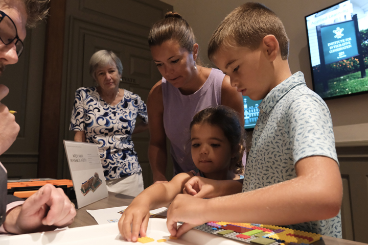 Two children pick up Lego bricks while adults look on.