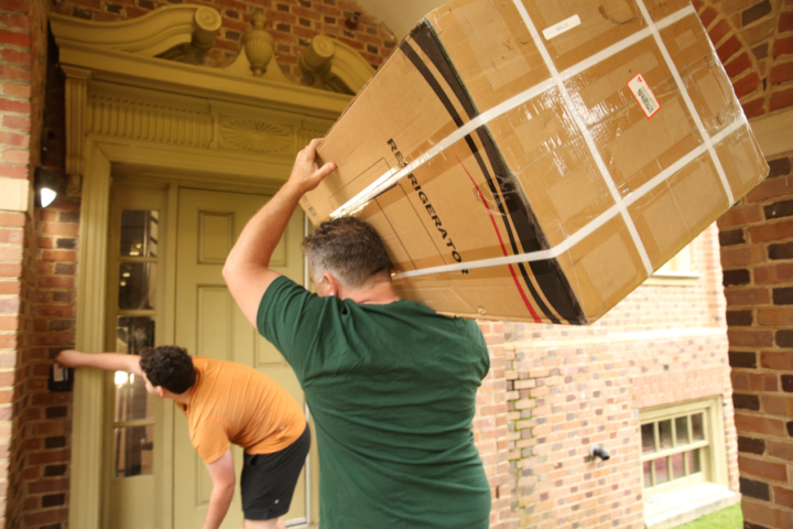 A person uses a card to open a door while another holds a refrigerator box on his shoulder.