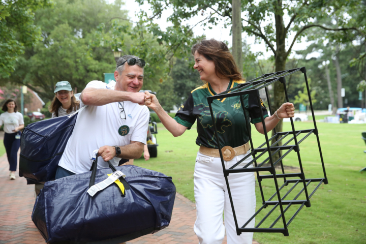 Two people fist-bump while carrying bags and shelves.