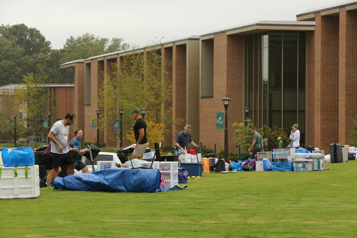 Piles of goods are lined up on a lawn outside of a large, brick building.