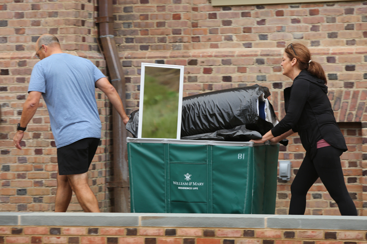 One person pulls and another pushes a cart filled with a mirror and other items.