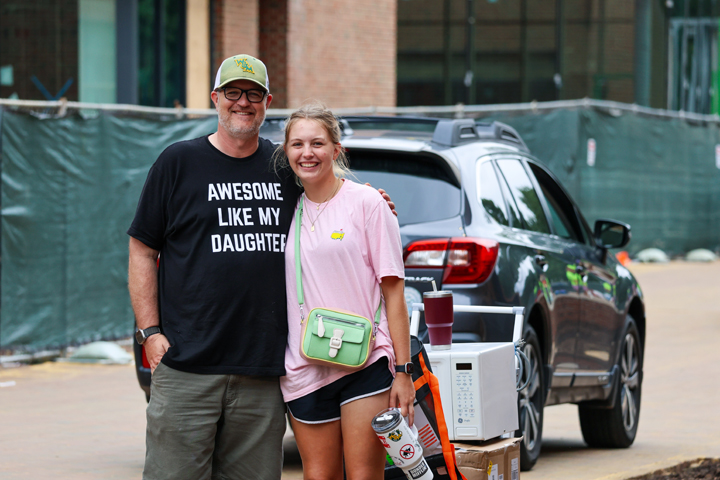 A dad wearing an "Awesome like my daughter" shirt poses for a photo with his daughter.
