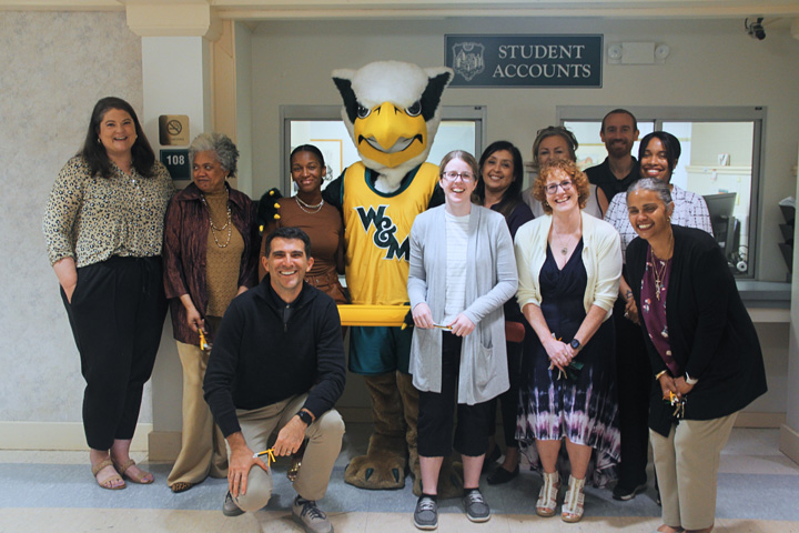 A person in a Griffin mascot holds an inflatable pencil and poses for a photo with people next to a brick building.