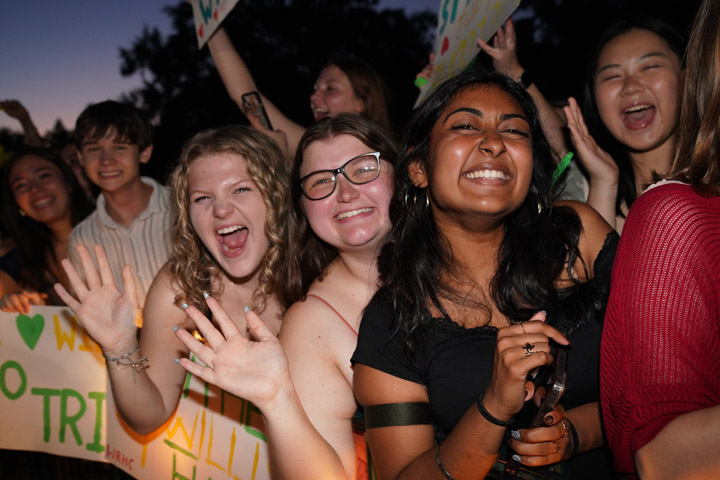 A group of people smile, wave and hold posters.