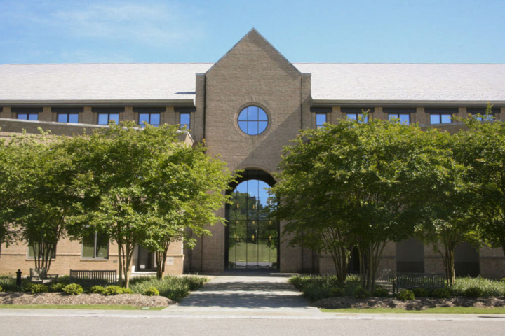The exterior of a large, brick building with a large archway entrance and circular window.