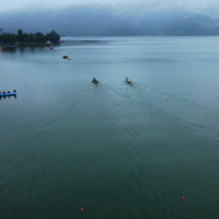 Gray skies appear over a body of water where people float in small boats.