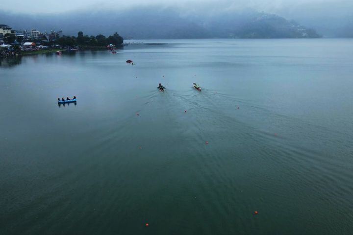 Gray skies appear over a body of water where people float in small boats.