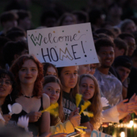 A person holds a Welcome Home sign while standing in a large crowd.