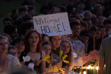 A person holds a Welcome Home sign while standing in a large crowd.