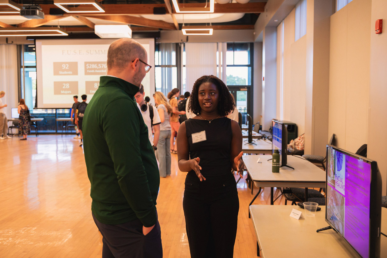 Two people talk near a table with a screen on it.