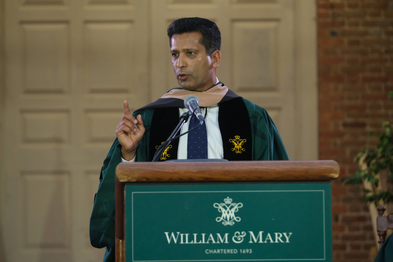 A person stands at a podium and speaks while wearing academic regalia.