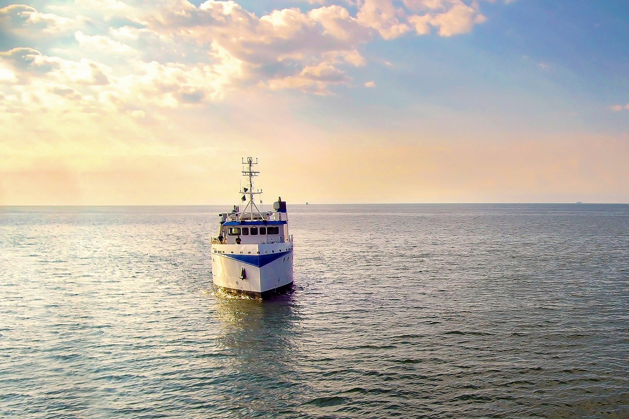 A ship floats on quiet waters as the sun sets in the background.