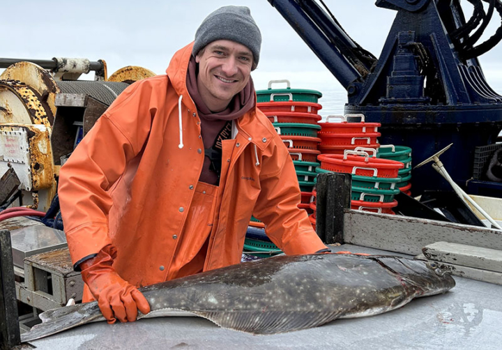 A person stands on a boat next to a large fish.