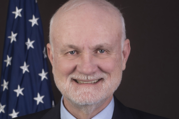 A headshot of Mark Christie with a U.S. flag in the background