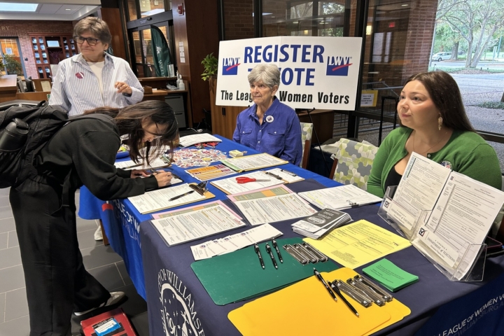 This is a photo of two volunteers and a Williamsburg voting official manning the voter registration table at W&M's law school while a law stud registers to vote
