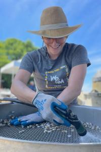 A person wearing gloves rinses shells over a grate.