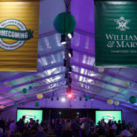 William & Mary and Homecoming banners hang from a ceoling of a large tent, in which people dance.
