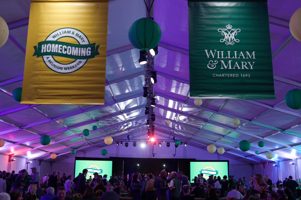 William & Mary and Homecoming banners hang from a ceoling of a large tent, in which people dance.