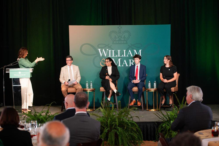 President Katherine Rowe stands at a podium and applauds four people sitting on a stage.
