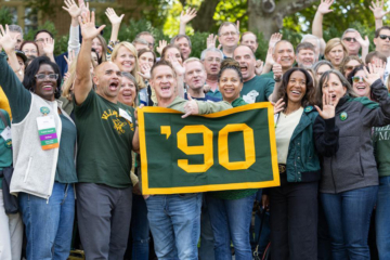 People smile and wave while holding a '90 sign.