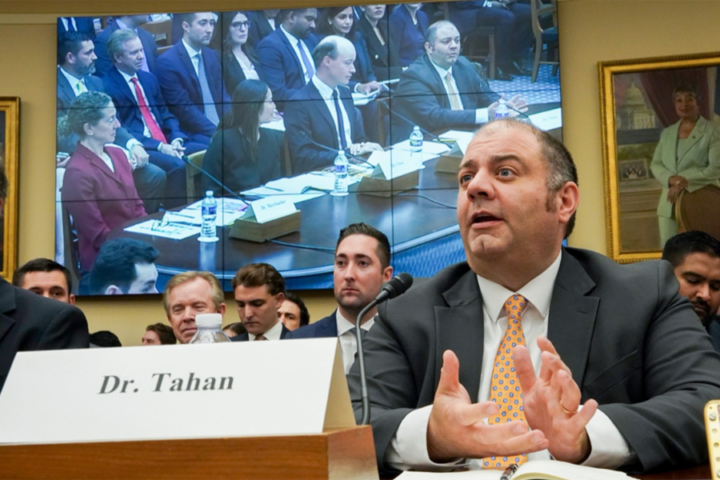 A person speaks at a table while other looks on.