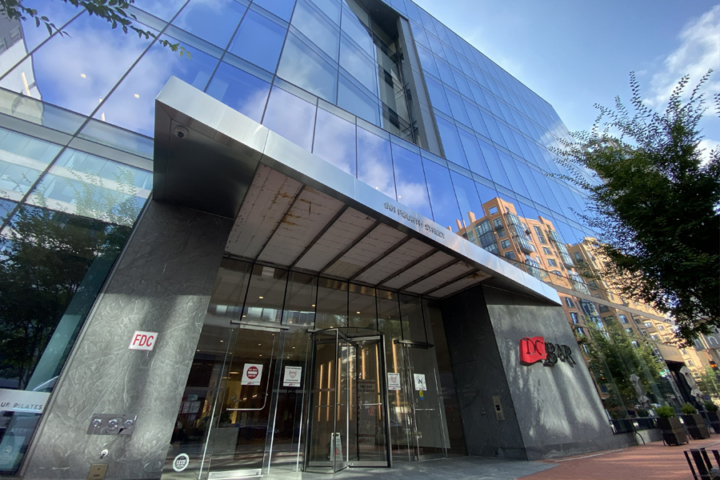 The exterior of a large office building with a covered door areas and a sign saying "DC Bar" on the side.