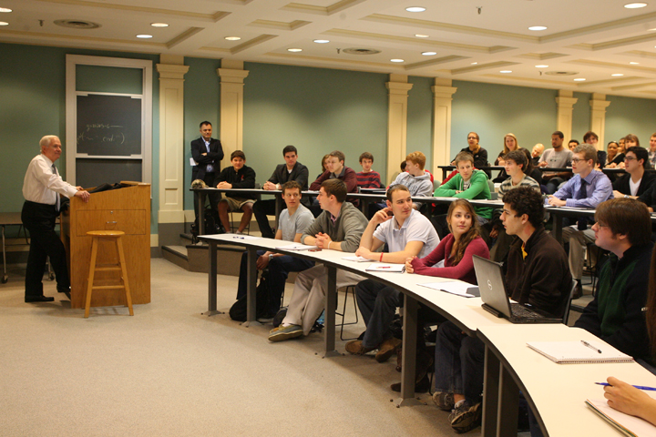 Robert Gates stands at a podium and looks out at a classroom of college students.