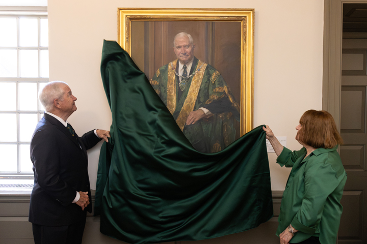 Two people pull a large, green sheet off of a portrait.