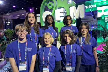 A group of seven people wearing William & Mary iGEM shirts post for a photo next to an iGEM sign.