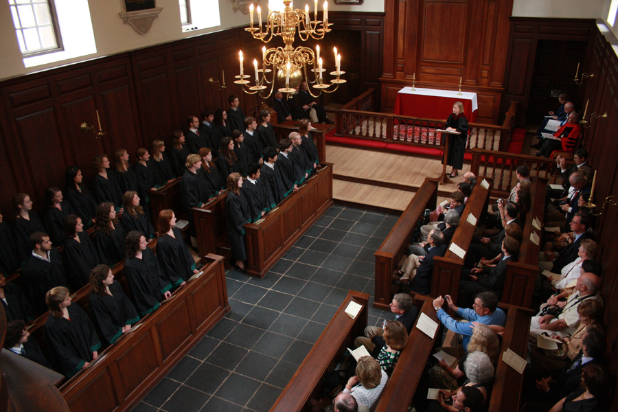 A view from a chapel balcony shows a group of people, some in graduation robes.