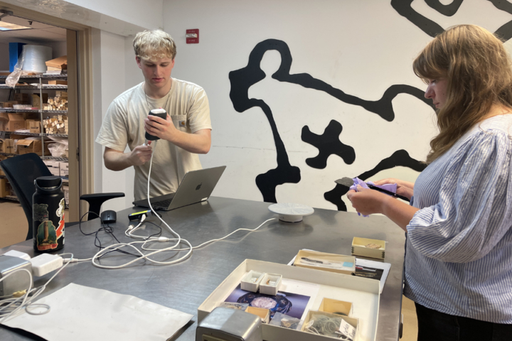A person holds an electronic device while another holds an artifact.