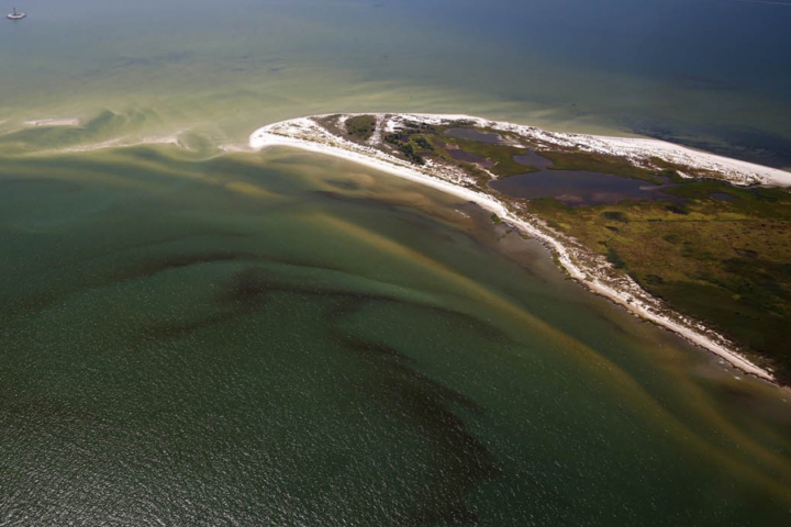 An aerial view of a body of water that shows swirls of red and lighters colors in the water.
