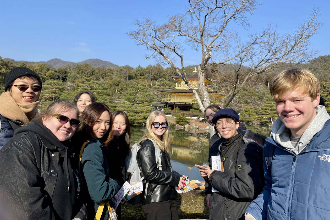 A group of people pose for a photo in front of a temple and body of water.